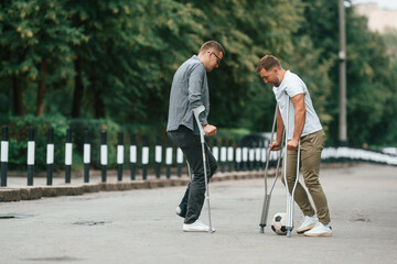 Obraz premium Playing soccer. Two men with crutches is outdoors on the road