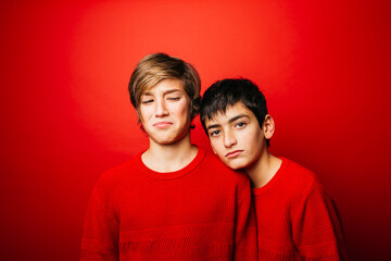Studio portrait of two pre-adolescent boys, wearing a red sweater, embracing over a red background