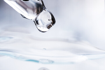A glass pipette with a close-up of cosmetic liquid on a gray background. Macro photography, side...