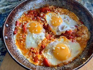 Fried eggs with stewed vegetables in a metal pan, top view