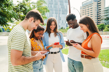 Multiracial group of young smiling students enjoying and having fun with their cellphones. Teenage friends sending text messages to each other on after class around campus. High quality photo