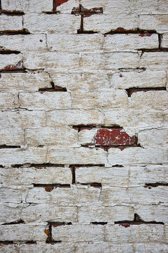 Red brick wall painted white with cracking paint and one exposed red brick