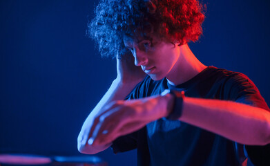 DJ is in the club. Young man with curly hair is indoors illuminated by neon lighting