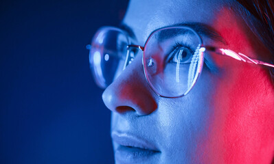 In glasses. Close up view. Young beautiful woman is indoors in the studio illuminated by neon light
