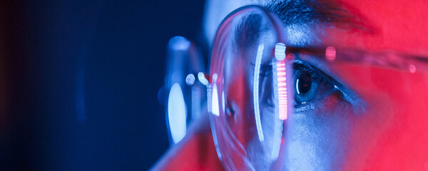 In glasses. Close up view. Young beautiful woman is indoors in the studio illuminated by neon light