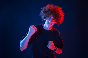 Feeling uplifting. Celebrating success. Young man with curly hair is indoors illuminated by neon lighting