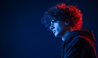 View from the side. Young man with curly hair is indoors illuminated by neon lighting