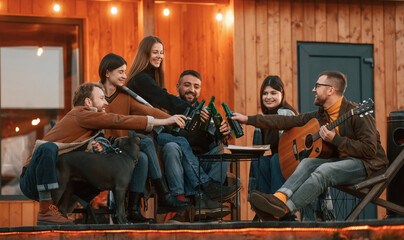 Positive emotions. Group of people is together near beautiful wooden building at evening time