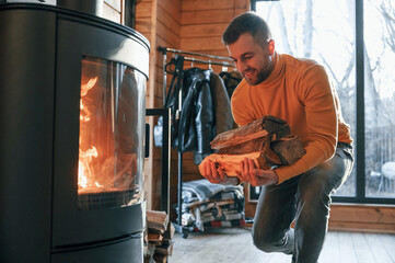 Man is putting wood into the fireplace indoors in the house