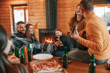 Playing guitar and talking. Group of friends is having good weekend indoors in the wooden building together