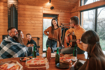 Playing guitar and talking. Group of friends is having good weekend indoors in the wooden building together