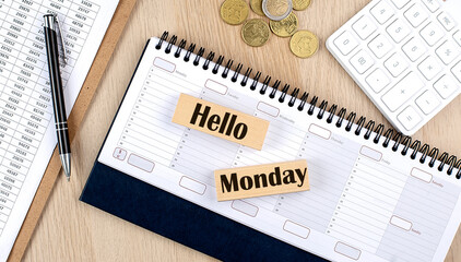 HELLO MONDAY word written on wooden block on planner with coins, clipboard and a calculator