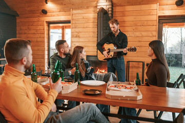 Beer, pizza and guitar. Group of friends is having good weekend indoors in the wooden building together