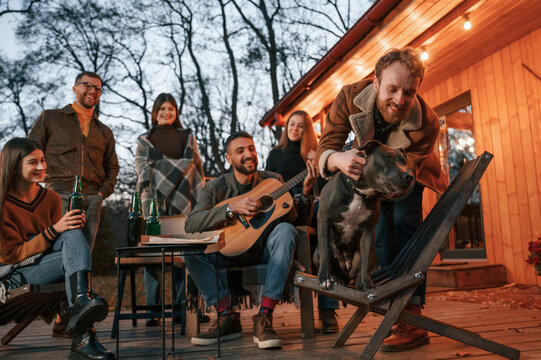 Everyone Is Looking At The Dog. Group Of People Is Spending Time Together On The Backyard At Evening Time