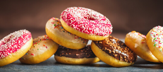 Set of different multicolored sweet donuts donuts with icing and sprinkles on a brown background