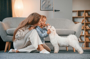 Giving the sweet meal to the animal. Mother with daughter is at home with maltese dog