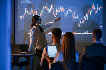 Showing the plan on the projector. Female leader talking to employees in office of stock exchange...