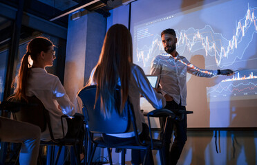 Trading teaching. Male leader talking to employees, showing the plan on the projector in office of...
