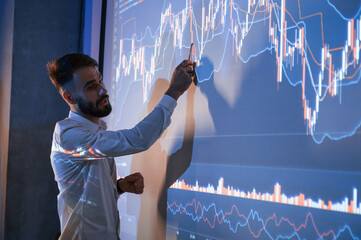 Man is standing near projector and showing graphs and business graphs
