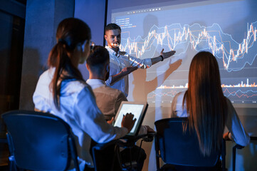 Speaking with audience. Male leader talking to employees, showing the plan on the projector in office of stock exchange company