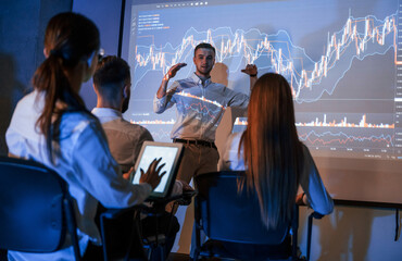 Speaking with audience. Male leader talking to employees, showing the plan on the projector in...