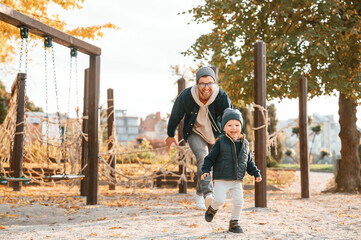 Fototapeta premium Running, having fun. Father and young son is together outdoors at daytime