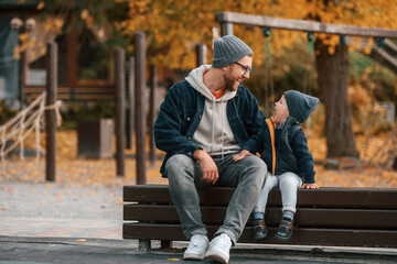 Obraz premium On the bench on playground. Father and young son are together outdoors at daytime