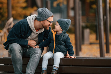 On the bench on playground. Father and young son are together outdoors at daytime
