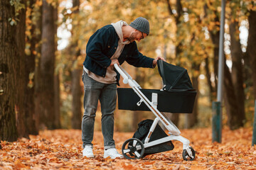 Looking inside the pram. Man is having a walk in the autumn park