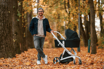 Standing and enjoying a nature. Man with pram is having a walk in the autumn park
