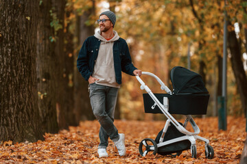 Obraz premium Front view. Man with pram is having a walk in the autumn park