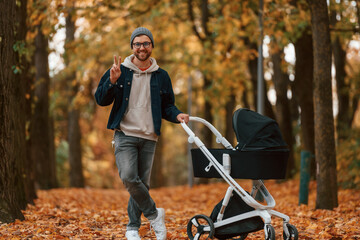 Front view. Man with pram is having a walk in the autumn park