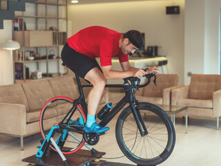 A man riding a triathlon bike on a machine simulation in a modern living room. Training during pandemic conditions.