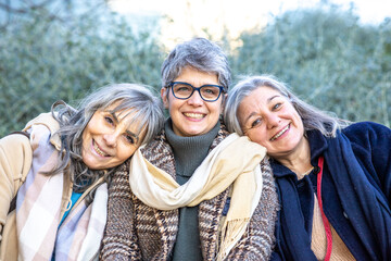 Happy group of mature women with gray hair hugging each other. Three senior female friends having...