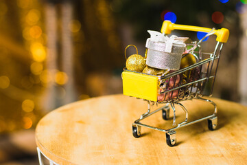 Christmas and new year spending concept. Christmas balls and a gift box in a shopping cart against a background of garlands and Christmas decorations.