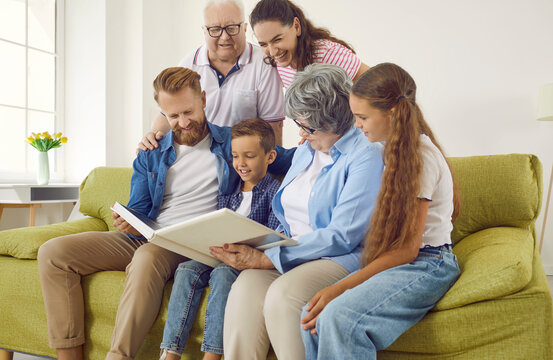 Happy big multigenerational family keep good memories of the past. Cheerful friendly smiling multi generational family sitting on the sofa in the living room and looking through a photo album together