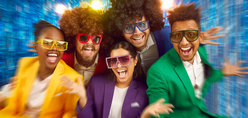 Portrait of laughing happy people in disco style sunglasses, colourful suits on blue blur...