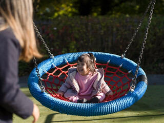 Mother and daughter with Down syndrome using swing on playground - obrazy, fototapety, plakaty