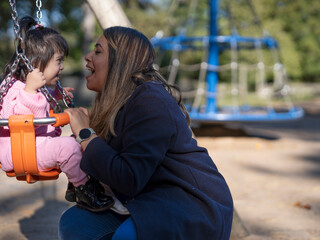 Mother swinging daughter with Down syndrome on playground swing - obrazy, fototapety, plakaty