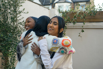 Three smiling women wearing hijabs greeting in garden