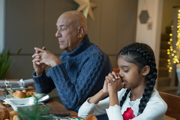Girl and grandfather praying during Christmas dinner