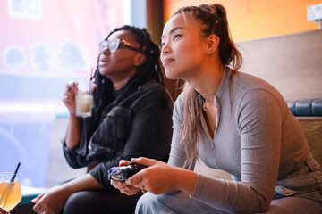 Female friends drinking cocktails and playing in video games at pub