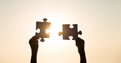 Silhouette two hands trying to connect couple puzzle piece.