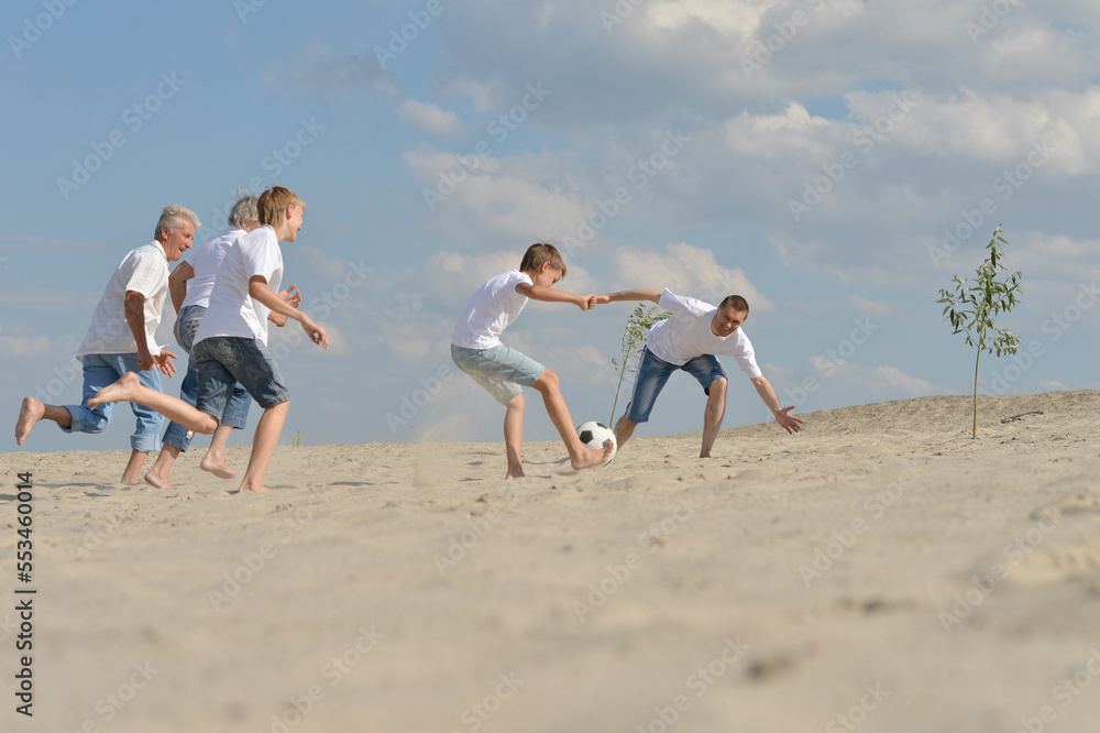 Wall mural Family playing football on a beach in summer day