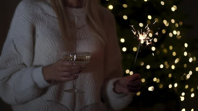 Celebrating Christmas or New Year eve party with Bengal lights and champagne. Close up of woman's hands holding glass of champane and sparkles.
A beautiful Christmas atmosphere at home.
