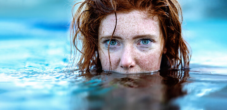 Portrait Of Sexy, Young Red Haired Woman With Freckles And Red Wet Hair, In Turquoise Spa Pool Water, Head Half Under Water