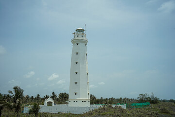 Fototapeta na wymiar A lighthouse on the beach painted white against a blue sky background