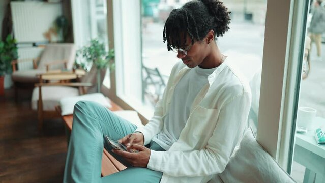 Positive African man with dreadlocks typing on phone in the cafe