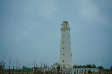 A lighthouse on the beach painted white against a blue sky background