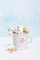 Marshmallows in shape of star in white cup with cocoa decorated with star on crochet napkin on bright blue background, studio shot, copy space